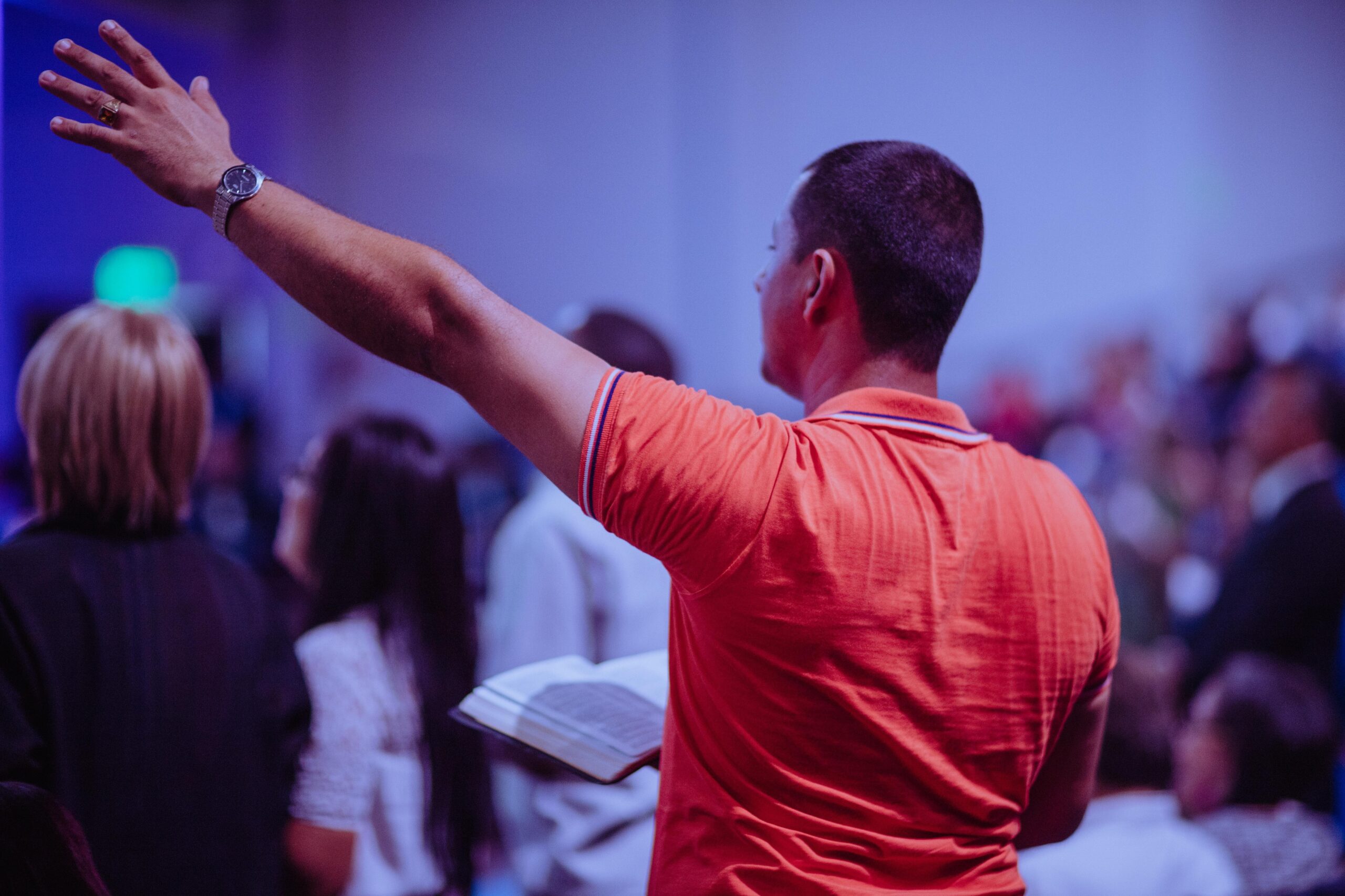 A man in an orange shirt holding his hand up.